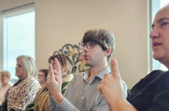 Employees sit together learning sign language in a workplace training session.